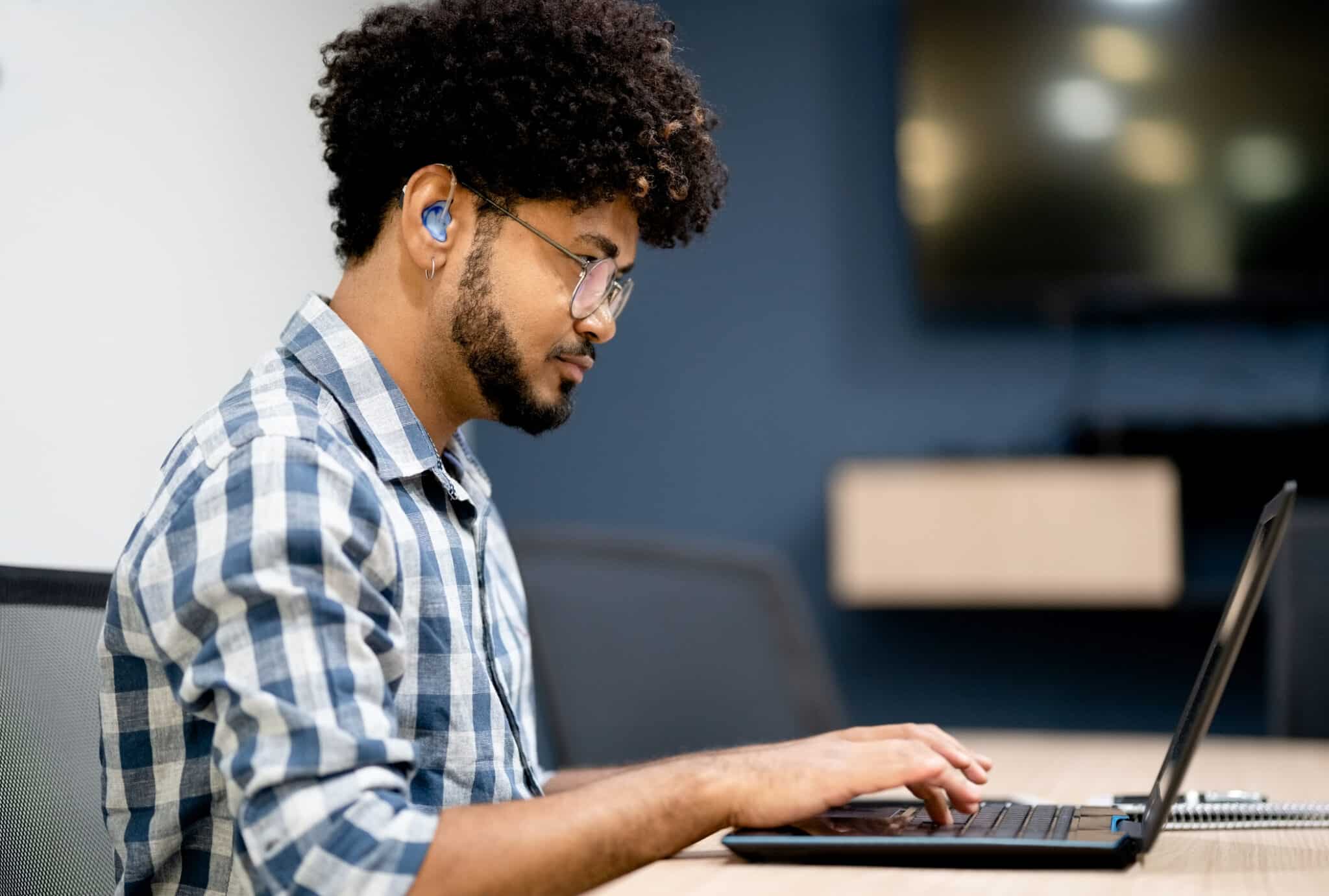 Side view of man with a hearing aid working on laptop at office