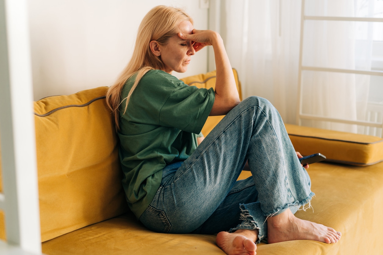 Anxious woman sitting on the couch holding her forehead.