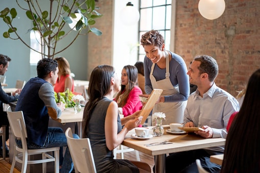 Couple dining in a crowded, noisy restaurant with a friendly server
