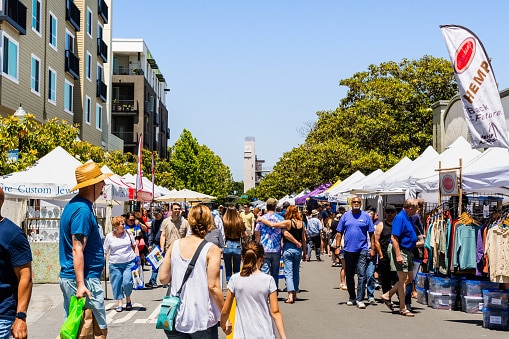 Large crowd of people browsing art and other wares at a street art fair on a beautiful summer day.